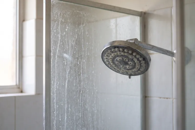 White limescale on an old shower head and the shower glass behind it